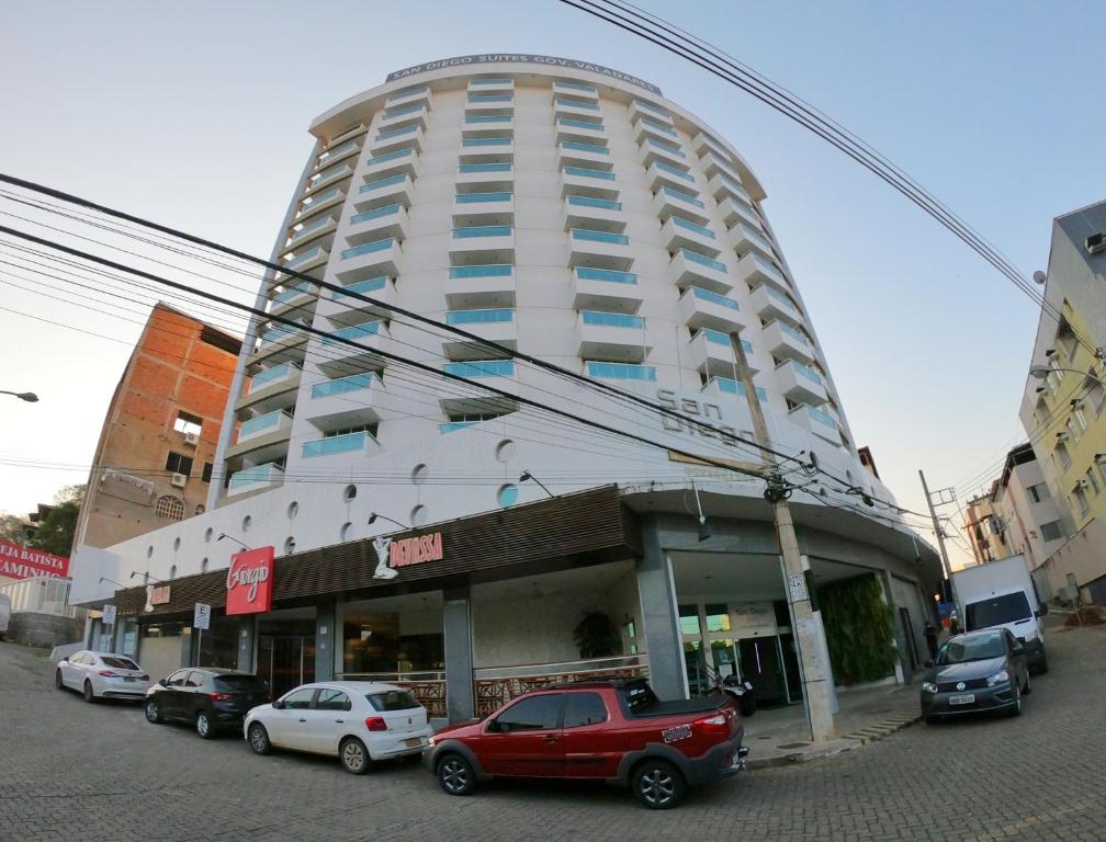 un gran edificio blanco con coches estacionados frente a él en TH Flats Governador Valadares, en Governador Valadares