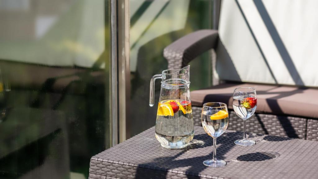 Glass pitcher with lemon and strawberry and two glasses on wicker patio table, sunlit relaxed setting