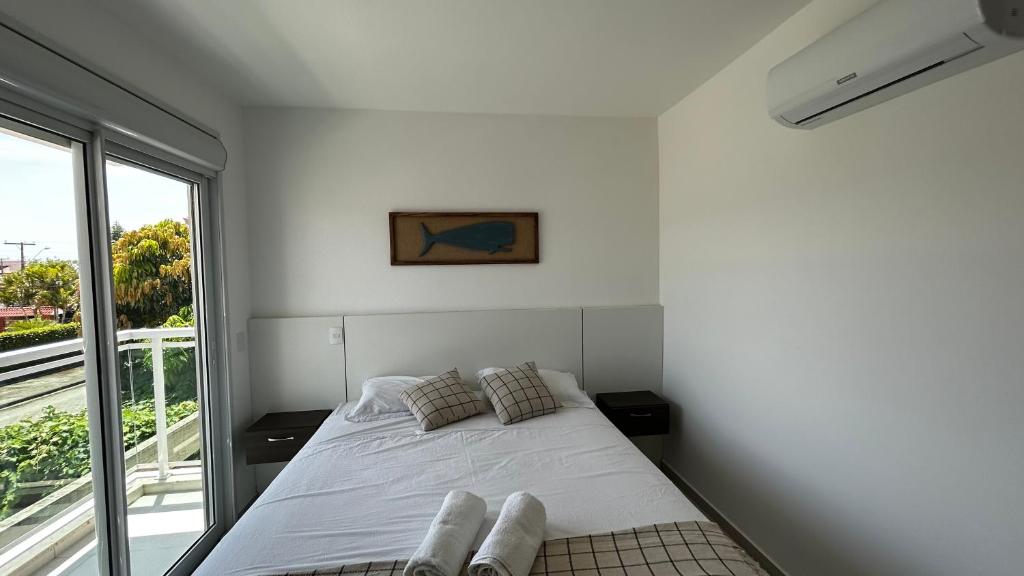 a white bedroom with a bed and a window at Casa em Floripa - 200m da praia in Florianópolis