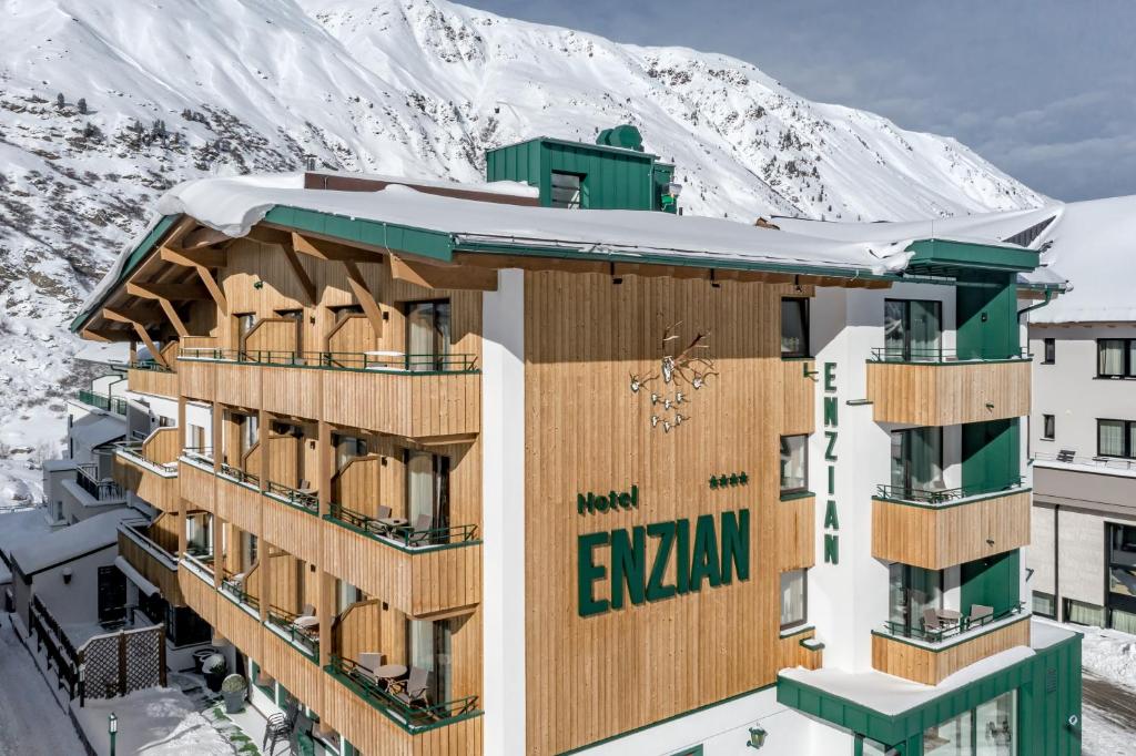 a building with snow covered mountains in the background at Hotel Enzian & Apartmenthotel Johannes in Obergurgl