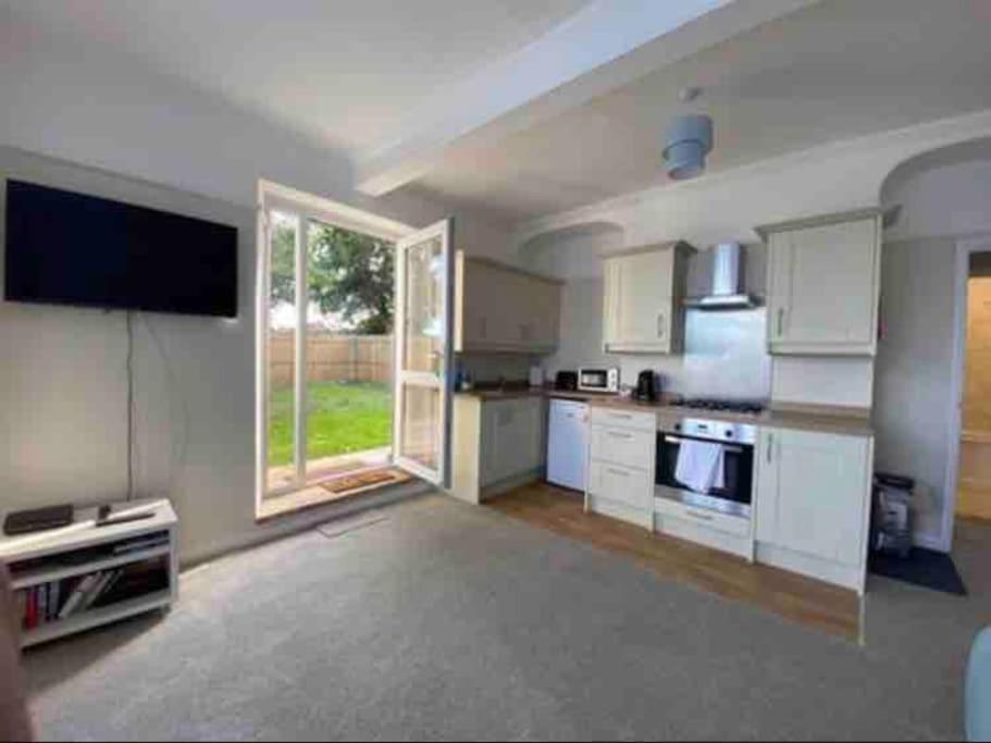 a kitchen with white cabinets and a large window at SeaBright; one bed apartment with garden and parking in Mundesley