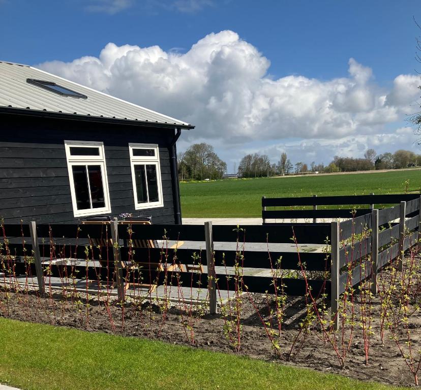 a black house with a fence next to a field at Woudmeer 1 in Dirkshorn