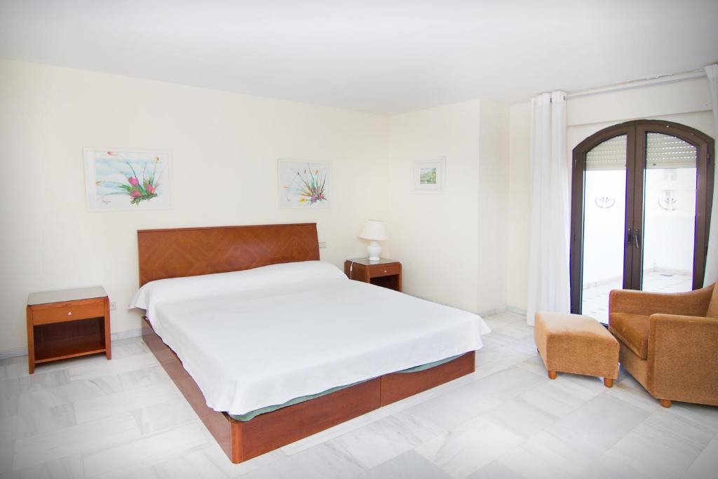 a white bedroom with a bed and a chair at Park Plaza Suites Apartamentos in Marbella