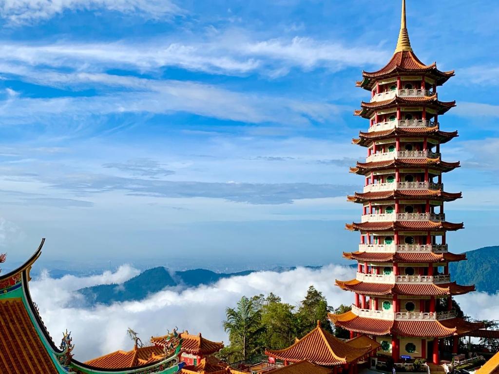 A breathtaking view of Genting Highlands, Malaysia, showcasing a mist-covered mountain resort with modern buildings, a colorful theme park, and lush greenery. The scene highlights the area's cool climate, scenic beauty, and vibrant attractions, making it a popular getaway destination