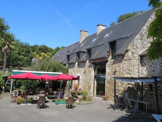 un edificio de piedra con mesas y sombrillas rojas delante de él en L'AUBERGE DE LA PORTE, en Saint-Jouan-des-Guérets