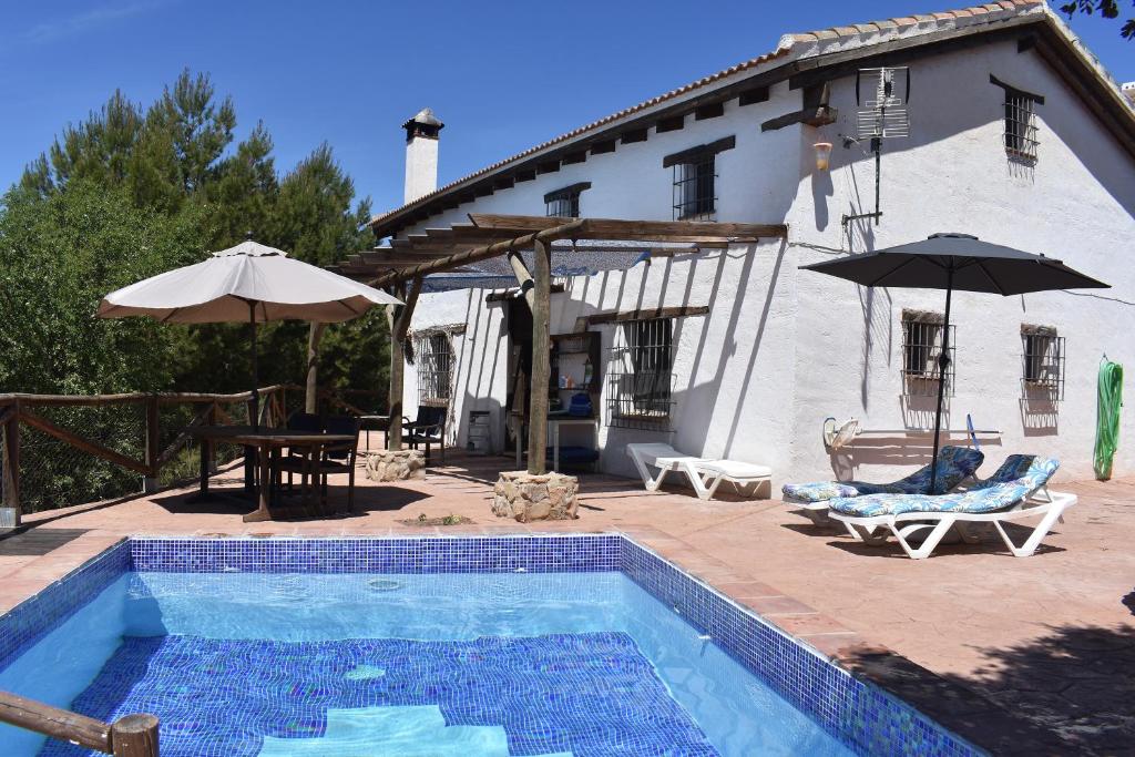 a swimming pool in front of a house with an umbrella at Casa KiSi Cottage, Rural Boutique Bed & Breakfast in Málaga