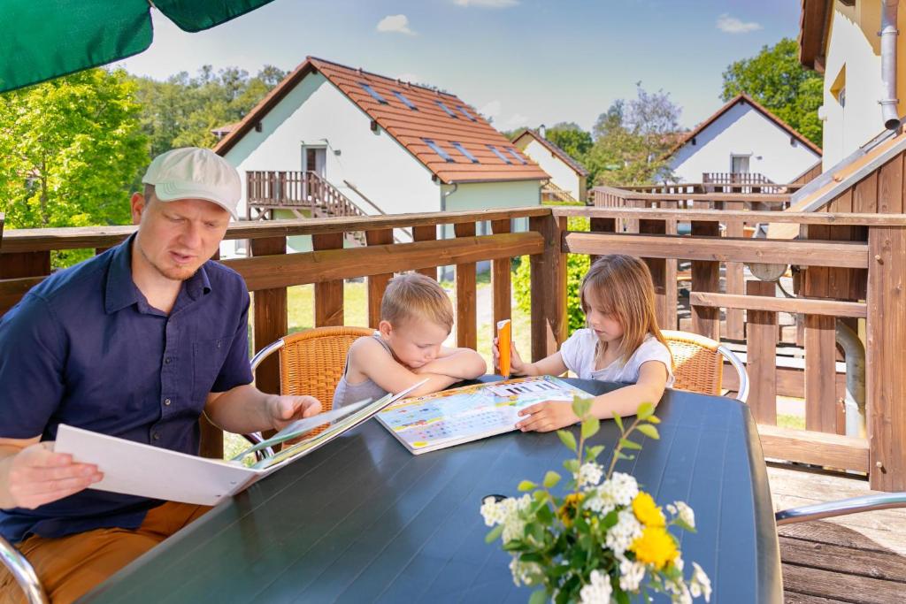 Ein Mann und zwei Kinder, die an einem Tisch sitzen und lesen in der Unterkunft Feriendorf Alte Fahrt in Rechlin