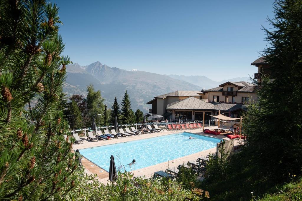 une grande piscine avec des chaises longues et un complexe hôtelier dans l'établissement SOWELL Family La Lauzière, à Aime La Plagne