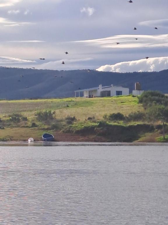 a house on a hill next to a body of water at Ou Werf Farm Cottage in Bredasdorp