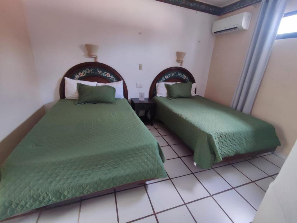 a bedroom with two beds with green sheets and a window at Hotel Rath in Campeche