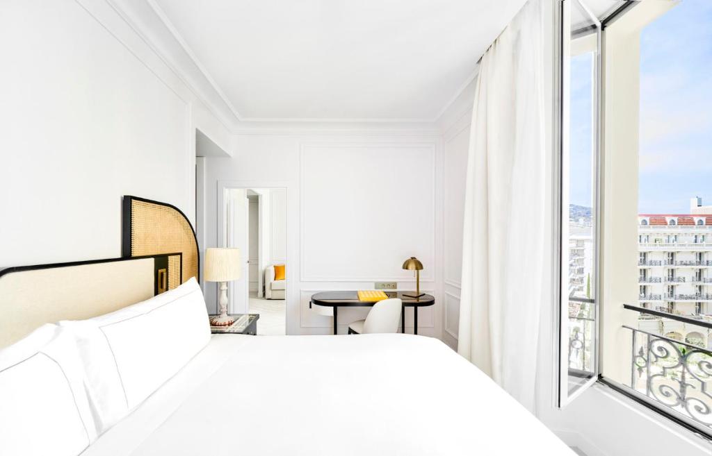 a white bedroom with a bed and a balcony at Carlton Cannes, a Regent Hotel in Cannes