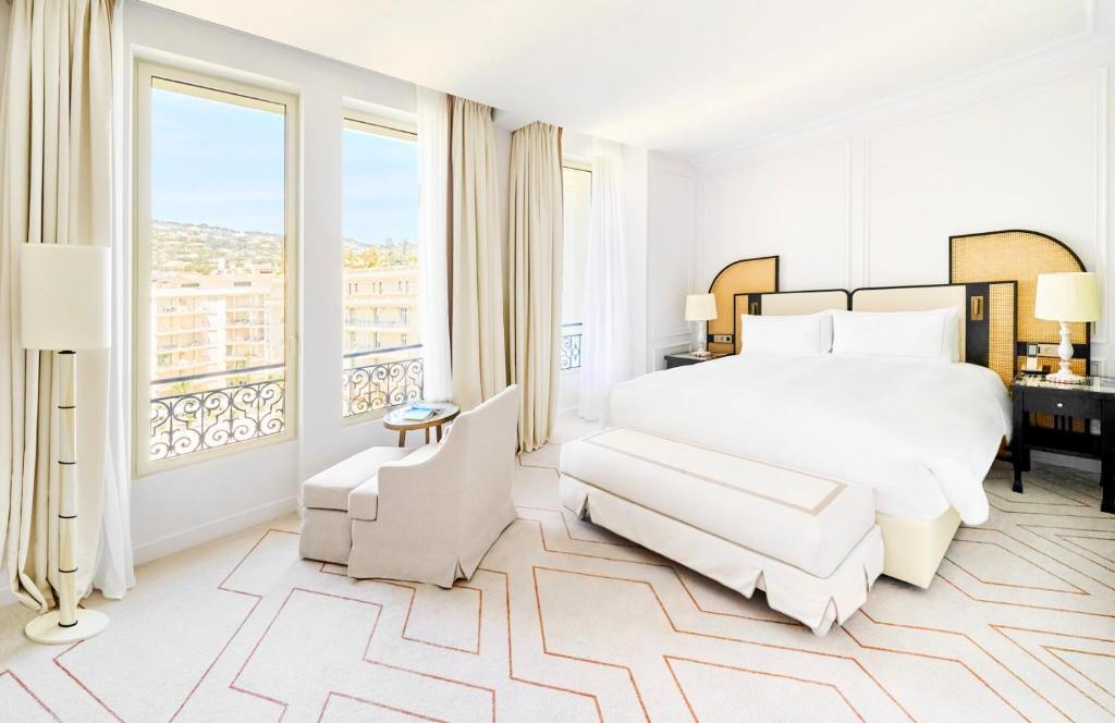 a bedroom with a white bed and a large window at Carlton Cannes, a Regent Hotel in Cannes