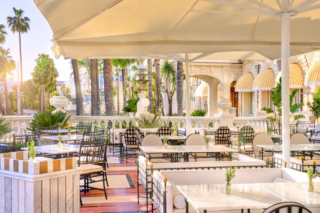 a restaurant with white tables and chairs and palm trees at Carlton Cannes, a Regent Hotel in Cannes