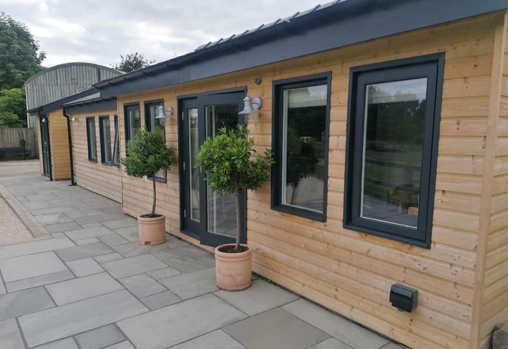 uma pequena casa com janelas e vasos de plantas num pátio em The Lodge em High Legh