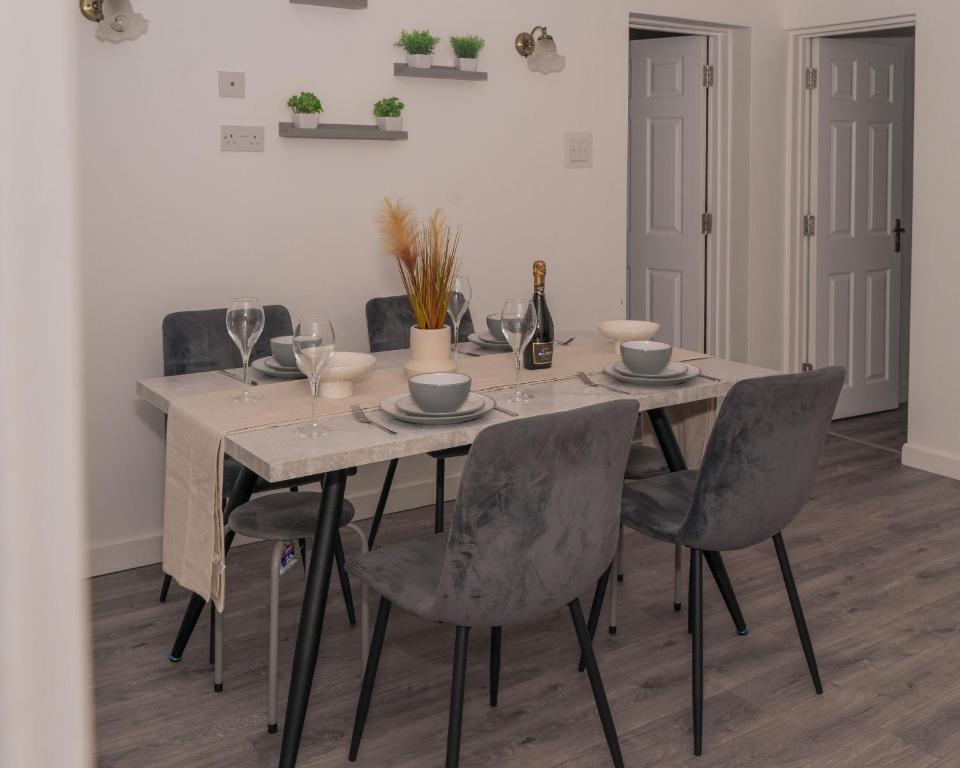 a dining room table with grey chairs and a table with wine glasses at Spacious 4 Bedroom Apartment in Coventry