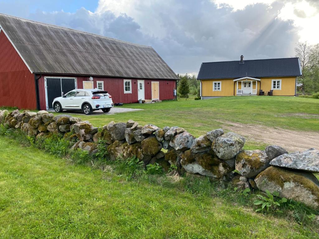 a stone fence in front of a barn and a car at Skog Fegen nära Ullared in Fegen