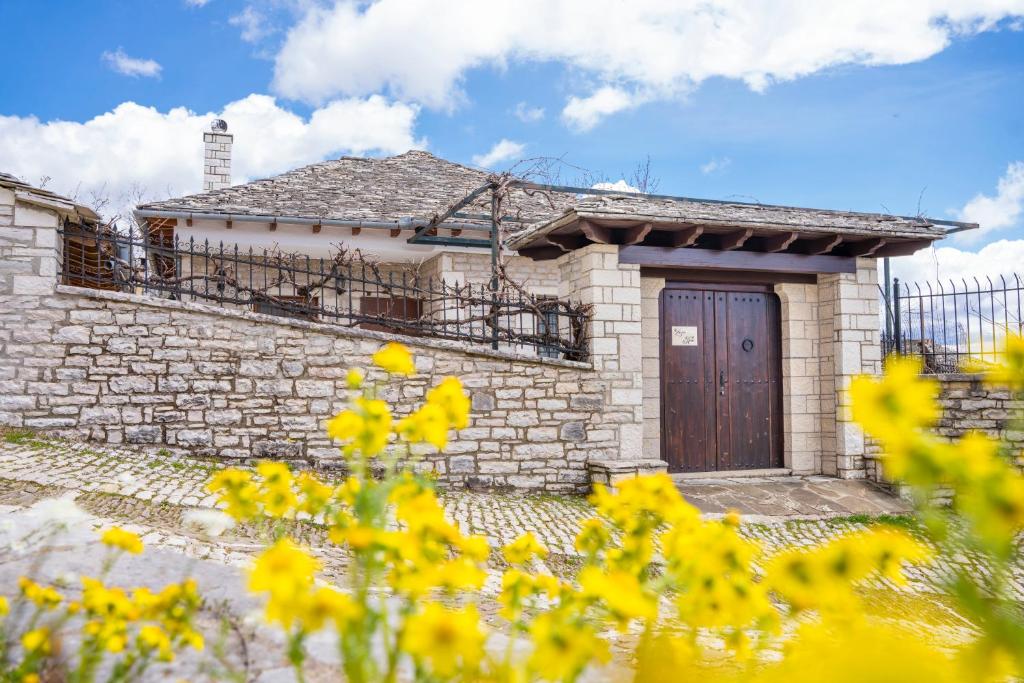 a brick house with a wooden door and yellow flowers at Zagori Home in Monodendri