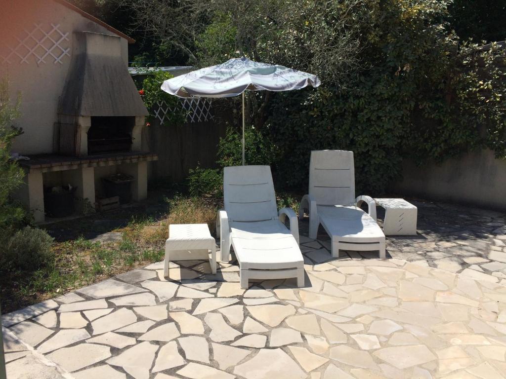 trzy krzesła i parasol na kamiennym patio w obiekcie La maisonnette des vacances w mieście Saint-Georges-dʼOléron