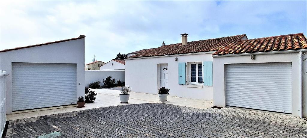 Una casa blanca con dos puertas de garaje. en Villa Ohana proche centre-ville, en Le Château-dʼOléron