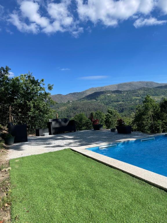 a swimming pool with a lawn and mountains in the background at Casa do Tapadinho in Ribeira de Pena