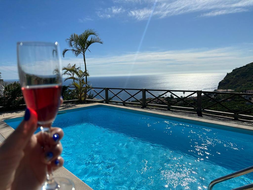 a person holding a glass of wine next to a swimming pool at Tropical Garden in Arco da Calheta