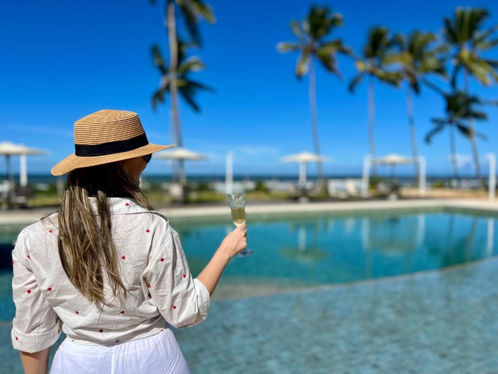 una mujer sosteniendo una copa de champán cerca de una piscina en Kalug - Duplex PÉ NA AREIA com 4 suítes, piscina e churrasqueira privativa na Praia do Sul! Perfeito para família - Wifi 300mb! en Ilhéus