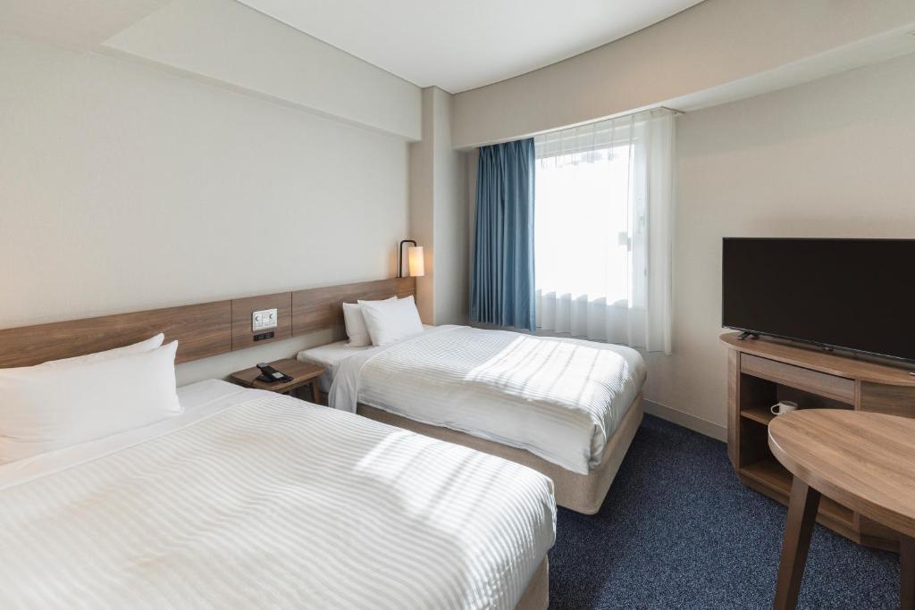 a hotel room with two beds and a flat screen tv at Sotetsu Fresa Inn Tokyo-Toyocho in Tokyo