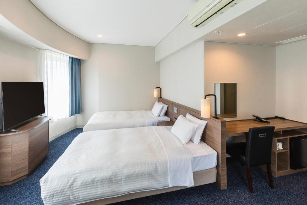 a hotel room with two beds and a desk and a television at Sotetsu Fresa Inn Tokyo-Toyocho in Tokyo