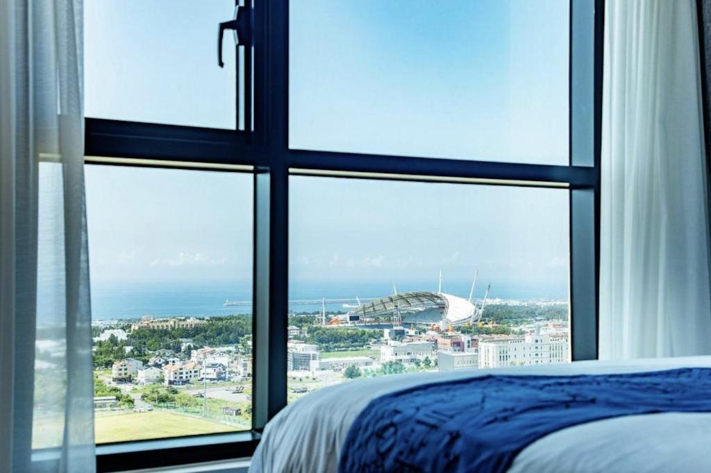 Schlafzimmer mit Blick auf ein Stadion durch ein Fenster in der Unterkunft Jeju Pureun Hotel in Seogwipo