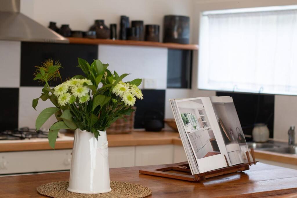 a white vase with flowers and a picture on a table at The Little House in Byron Bay