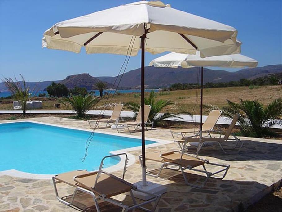 un gruppo di sedie e un ombrellone accanto alla piscina di Studio at beautiful beach Kouremenos a Anevató