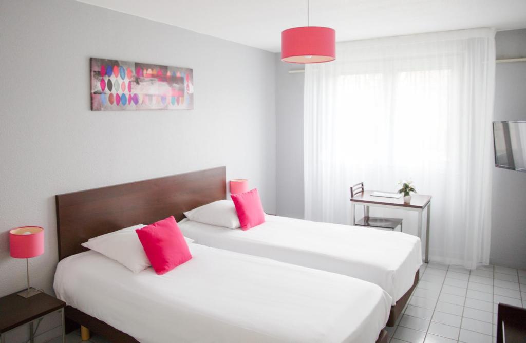 a bedroom with two white beds with red pillows at Zenitude Hôtel-Résidences La City in Besançon