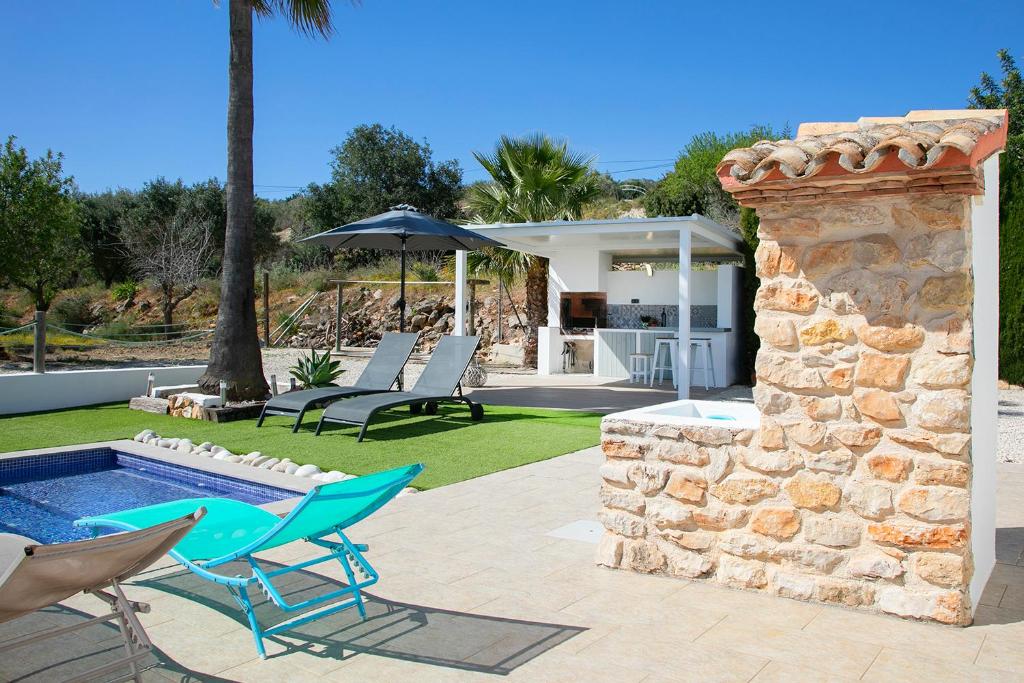 un patio trasero con piscina, sillas y pared de piedra en FINCA ROMER, en Benissa