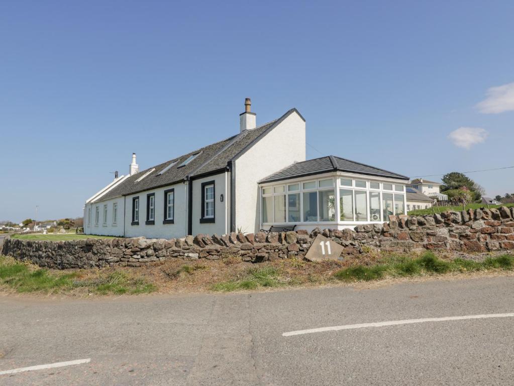 uma casa branca com uma parede de pedra ao lado de uma estrada em Ailsa Shores em Turnberry