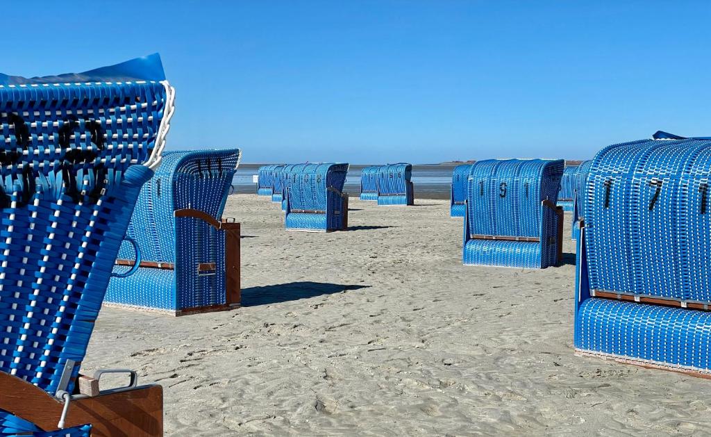 uma fila de cadeiras de praia azuis na praia em Ferienwohnung direkt am Deich - Seerobbe - em Dornum