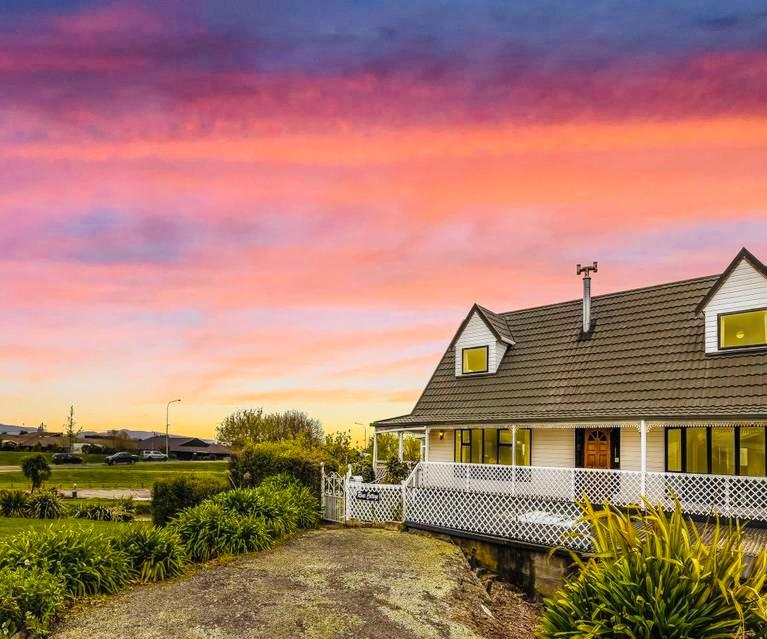 a white house with a sunset in the background at River Cottage in Blenheim