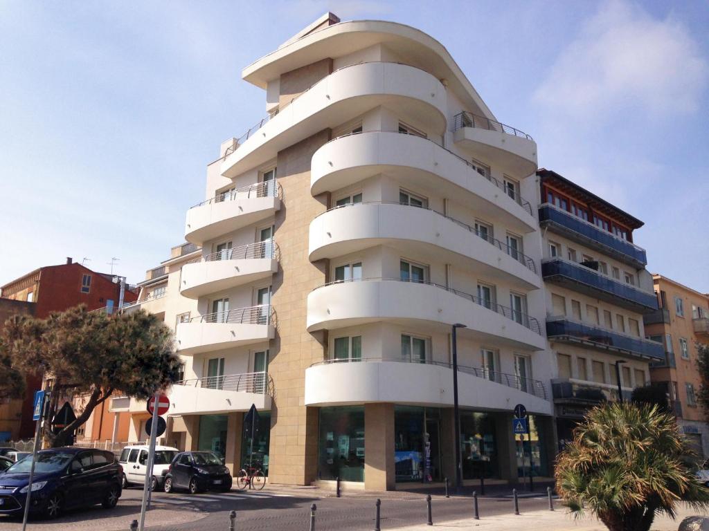 un alto edificio bianco con macchine parcheggiate di fronte di Residenza Roma Marina a Sottomarina