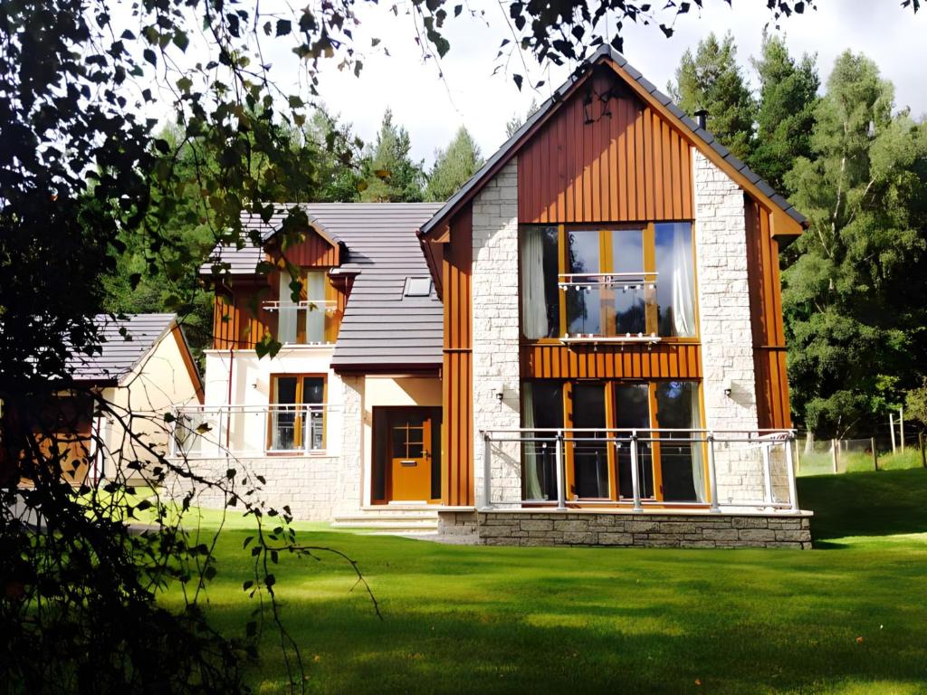 a house on a grassy field with trees at Carn Mhor Lodge in Aviemore
