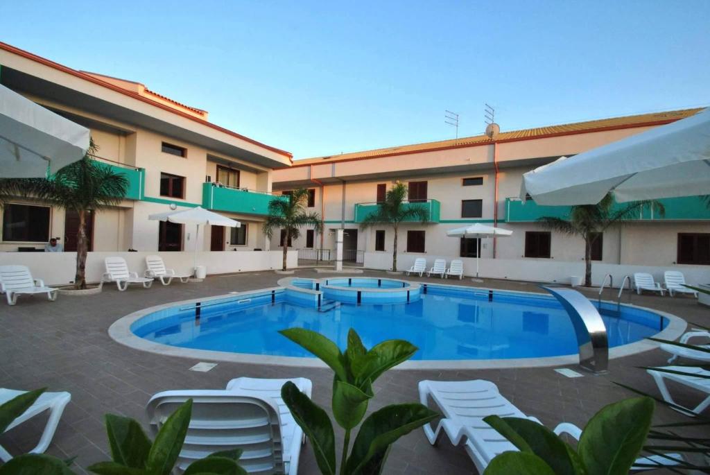 una piscina di fronte a un hotel con sedie bianche di Residence Fronte Mare a Santa Maria del Focallo