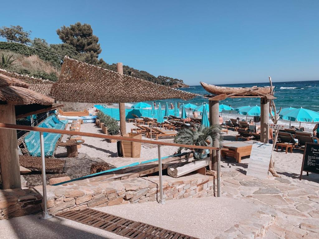 a beach with tables and umbrellas and the ocean at Hôtel La Villa Douce in Rayol-Canadel-sur-Mer