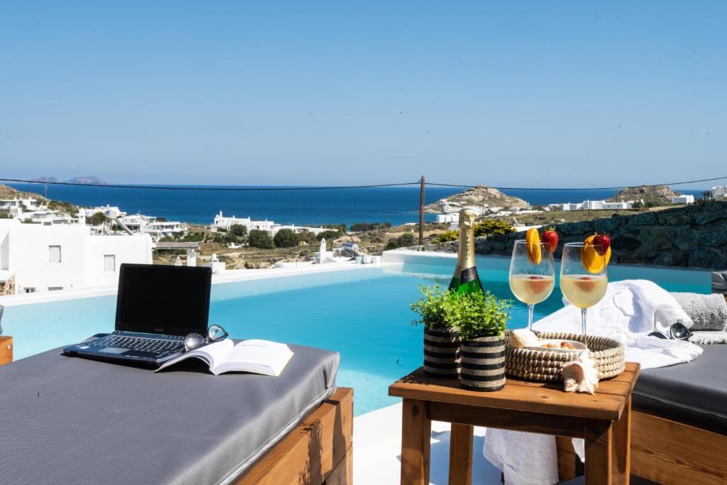 a table with a laptop and wine glasses next to a pool at Amma Houses Sea View in Kalafatis