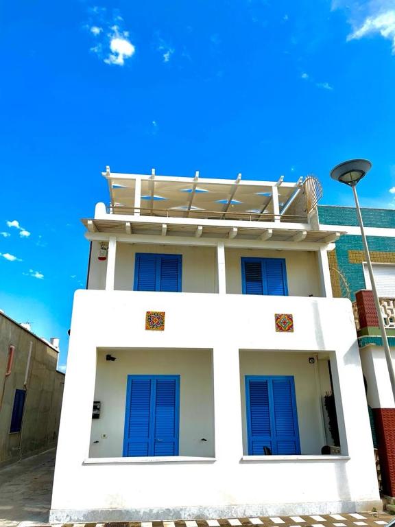 a white building with blue windows and a blue sky at HOLIDAY HOME AURORABIO- locazione turistica breve in Tre Fontane