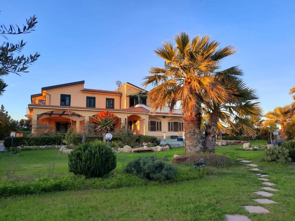 a palm tree in front of a large house at Hostel Vela Vega in Butera