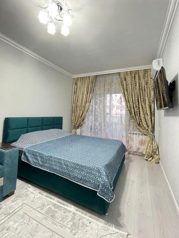 um quarto com uma cama azul e uma janela em 1-комн ЛЮКС в ЖК OTAU City em Shymkent