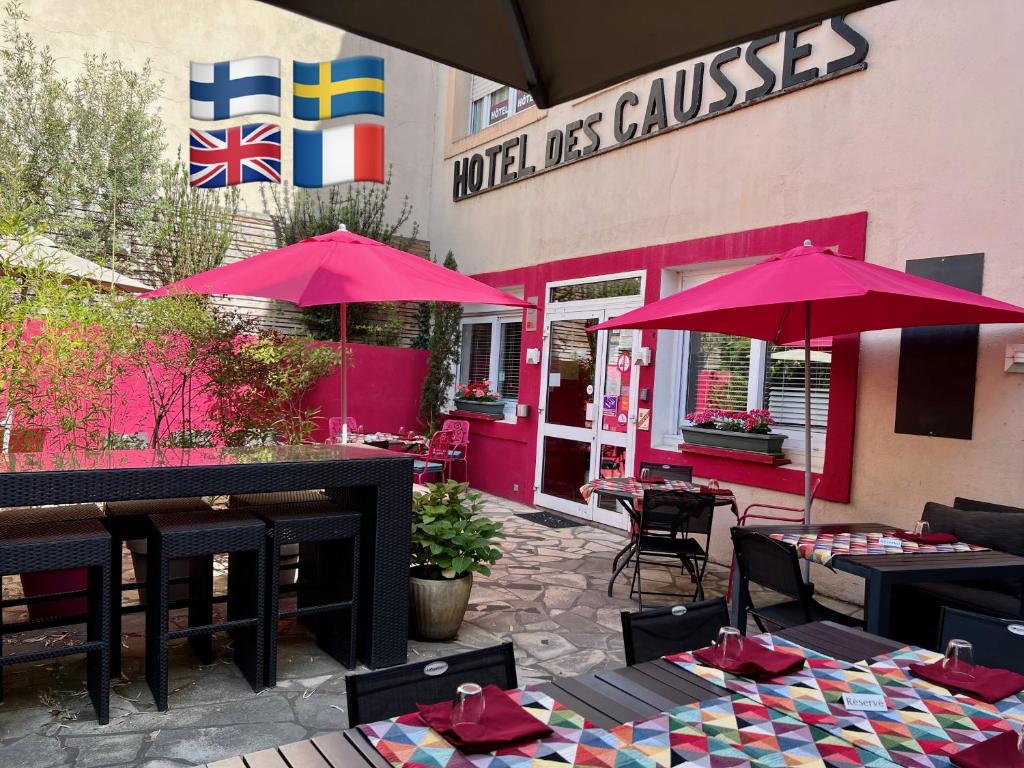 un restaurante con mesas y sombrillas frente a un edificio en Logis Hôtel des Causses, en Millau