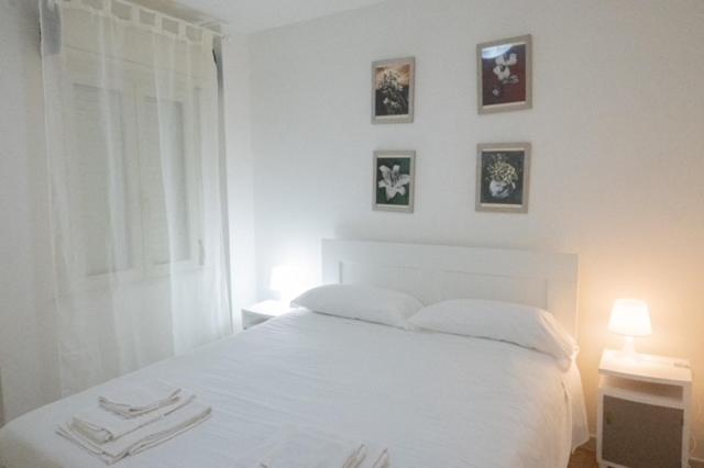 - un lit blanc dans une chambre avec des photos sur le mur dans l'établissement Villanova Apartment, à Cagliari
