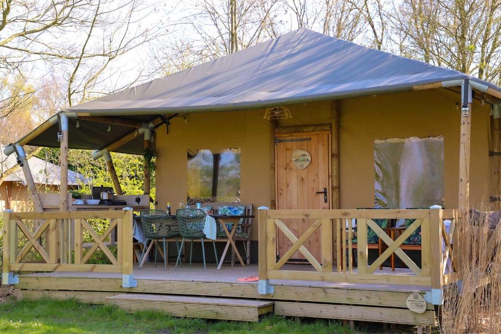 una pequeña casa amarilla con porche y mesa en Glamping Safarilodge 'Grutte Fiif' met airco, extra keuken op veranda en privé achtertuin en Grou