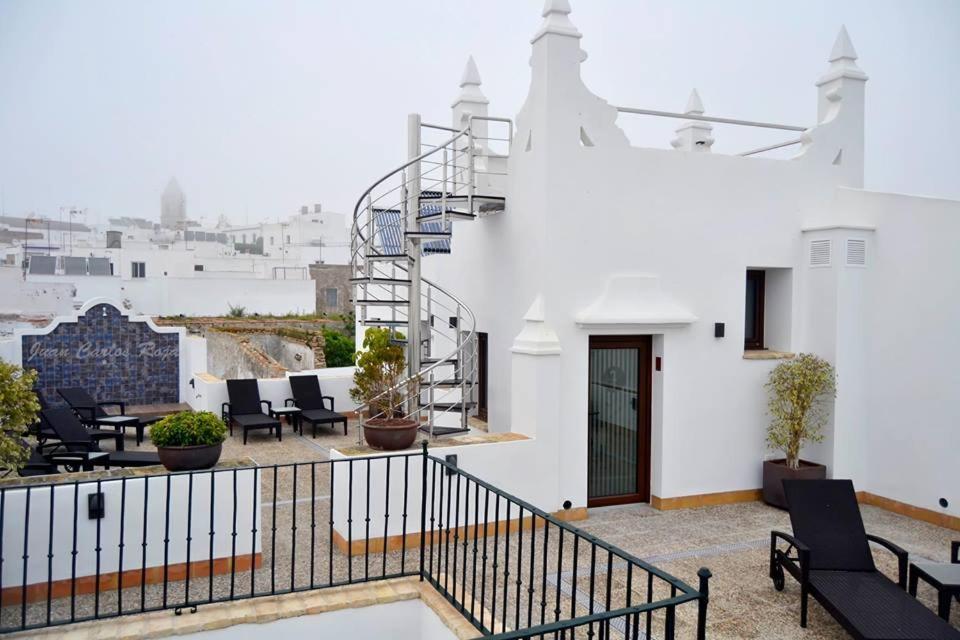 a white building with chairs and a staircase on a balcony at Ferreira Hostal Boutique in Conil de la Frontera