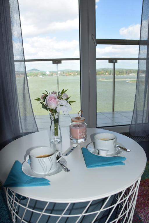a table with two cups and a vase with flowers at Panorama Apartman in Velence