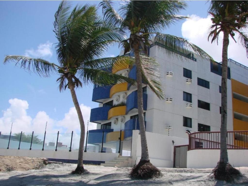 un edificio en la playa con palmeras delante en Apartamento Pé Na Areia - Praia do Bessa - PB en João Pessoa